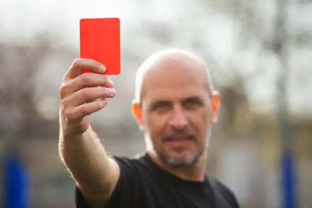 Mid-shot of amateur football match referee sending off player by showing red car in local tournament