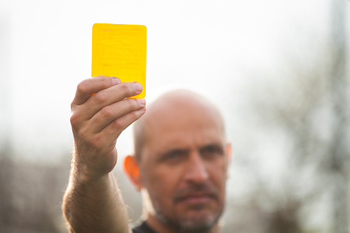Mid-shot of amateur football match referee warning player by showing yellow card in local tournament
