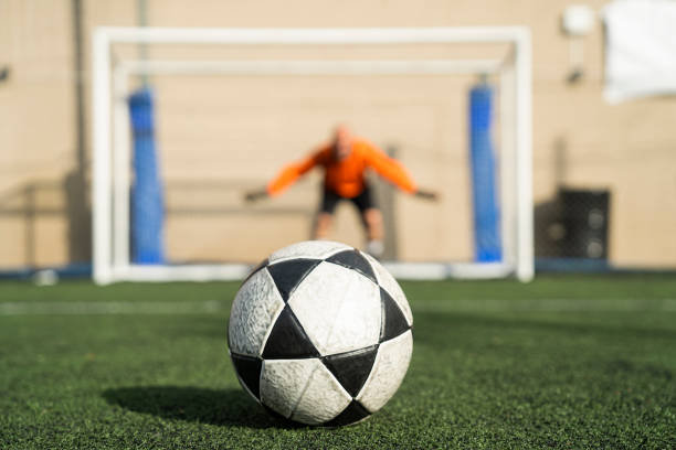 Full-length image of young man, soccer player in orange uniform hitting ball with chest isolated over white background with grass flooring. Concept of sport, game, competition, active lifestyle