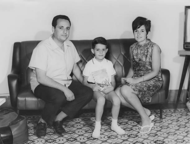 foto en blanco y negro tomada en los años 60, pareja posando con su hijo sentado en el sofá de su sala de estar - spanish and portuguese ethnicity fotos fotografías e imágenes de stock