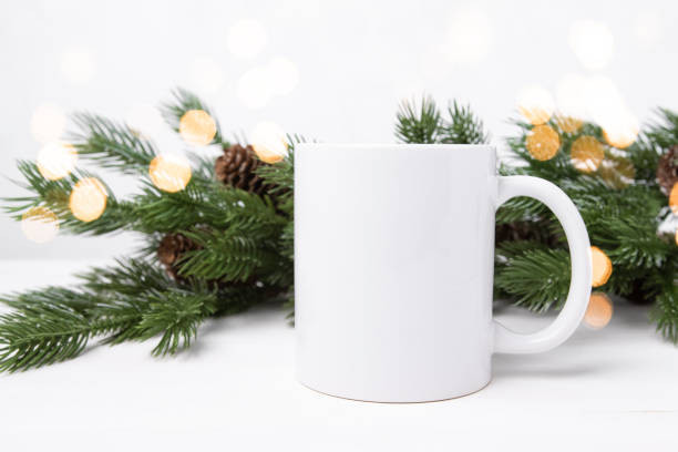 istock Mockup of a white ceramic cup on a table with spruce branches and defocus lights. Template for applying text and logo. 1436606079