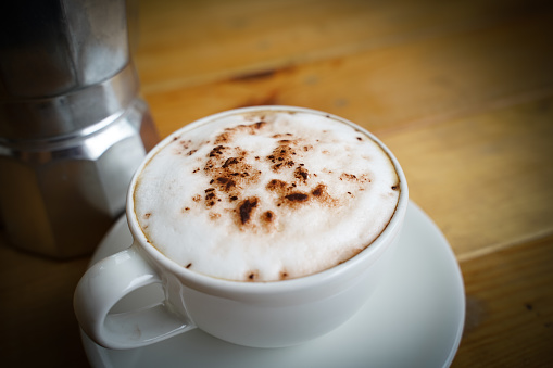 Hot cappuccino in white cup with wooden background,coffee is a popular drink all over the world.