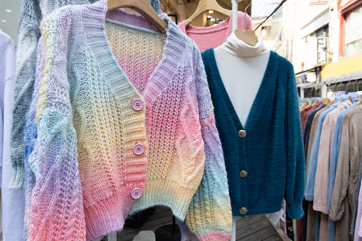 A shopping rank filled with clothes, colorful knited sweters. Bunch of clothes of different colors for sale. Cheep clothing and fast fashion theme