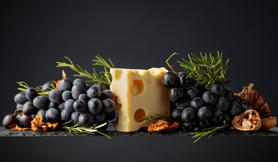 Maasdam cheese with walnuts, blue grapes, and rosemary on a black background.