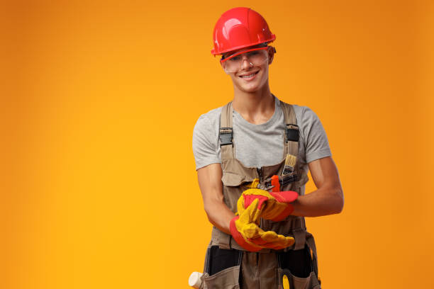 istock Young construction worker in helmet and uniform posing on yellow background in studio 1436616819