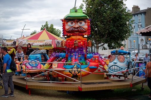 Bray, Ireland – August 01, 2022: Colorful carousel with toy vehicles as seats at the Seafront Fun Fair annual event in Bray, Ireland. Cloudy summer day.
