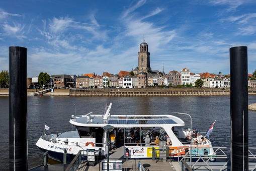 Deventer, Netherlands – August 10, 2022: Ferryboat waiting for passengers to transport across the river IJssel with cityscape of Hanseatic city Deventer in the background