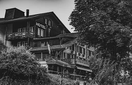 Lauterbrunnen, Switzerland – September 19, 2022: A grayscale Monochromatic image of a mountainside hotel in Lauterbrunnen surrounded with trees