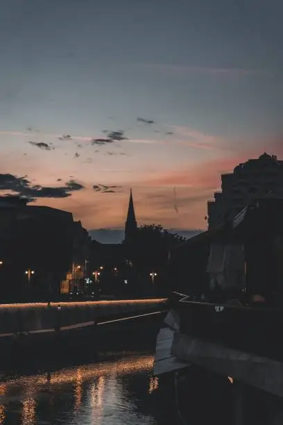 Photo of Vertical shot of a silhouette of a tower seen in the distance during sunset by a river