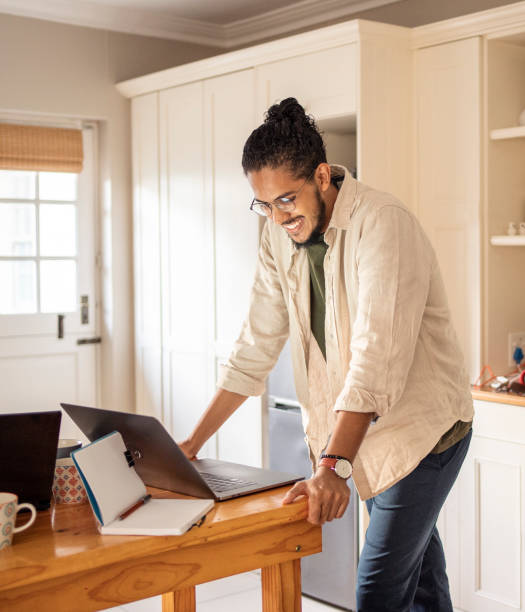 istock Smiling young man leaning on at a desk and working on a laptop 1436624055