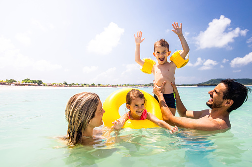 Young happy parents and their kids having fun during summer day in the sea.