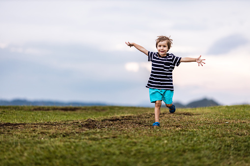 Cute little boy having fun while running with his arms outstretched in nature. Copy space.