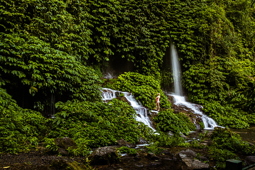Young happy woman enjoying by the waterfall in the rainforest. Copy space.
