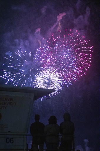 Three people looking up on colorful fireworks at night