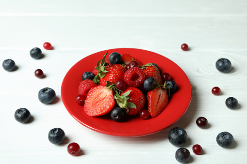 Plate with berry mix on white wooden background