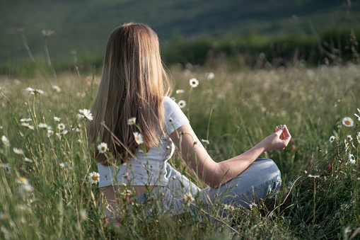 Beautiful young woman with long blonde hair meditates in nature, in a beautiful field. Travel and healthy lifestyle, enjoying nature