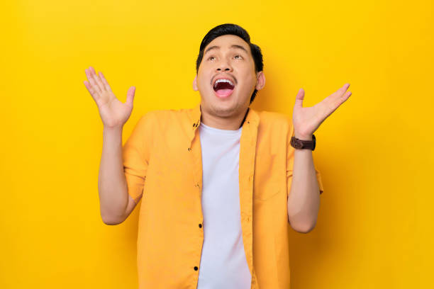 istock Surprised young handsome Asian man looking upward with raised hands isolated on yellow background 1436646383