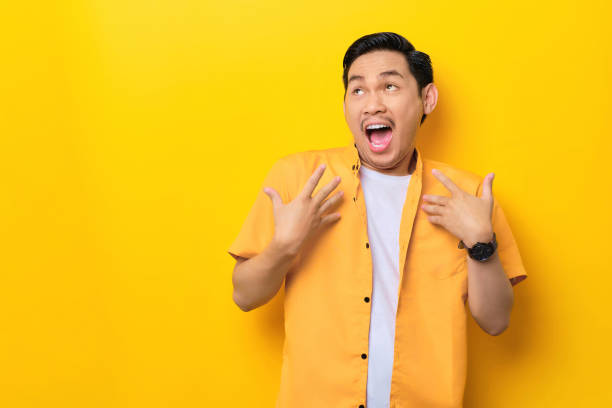 istock Surprised young handsome Asian man keeps hands on chest opened mouth isolated on yellow background 1436646388