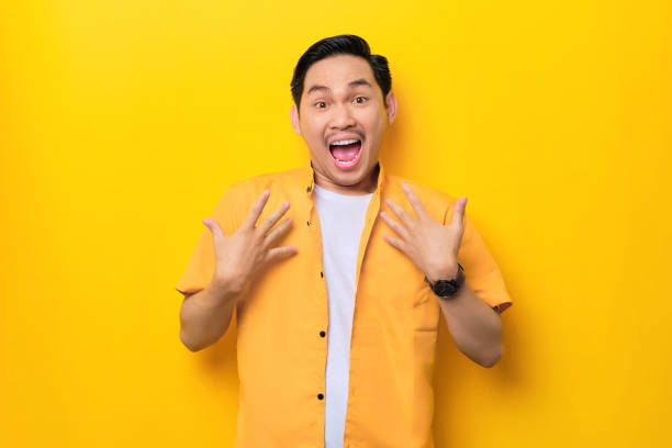 istock Surprised young handsome Asian man keeps hands on chest opened mouth isolated on yellow background 1436646401