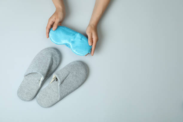 istock Female hands holds sleep mask on gray background with slippers 1436651383