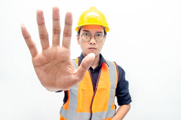 young asian male construction worker or engineer using yellow helmet and orange vest refuse and reject something. asian male worker crossed hand makes stop gesture isolated over red background. helmet hardhat protective glove safety stock pictures, royalty-free photos & images