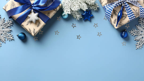 istock Christmas frame top border made of fir tree branches, gift boxes, silver blue stars, balls over blue background. Flat lay, top view. Xmas banner mockup 1436656095