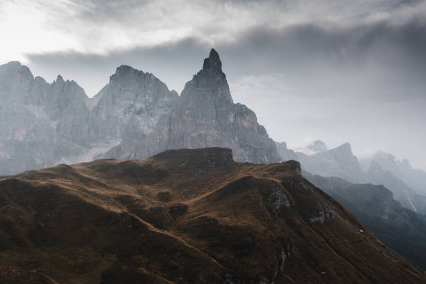 The low clouds create a dramatic scene in this stunning part of the Dolomites mountains. The clouds are slowly drifting across the hills, revealing the peaks in the distance. The sun is rising which allows the rays to fight through the clouds, creating stunning rays of sunshine.