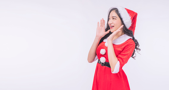 Excited asian woman wear red Santa Claus, Christmas hat holding hands open mouth screaming wow looking copy space over isolated white background. Cheerful surprised young girl Santa Claus excitement.