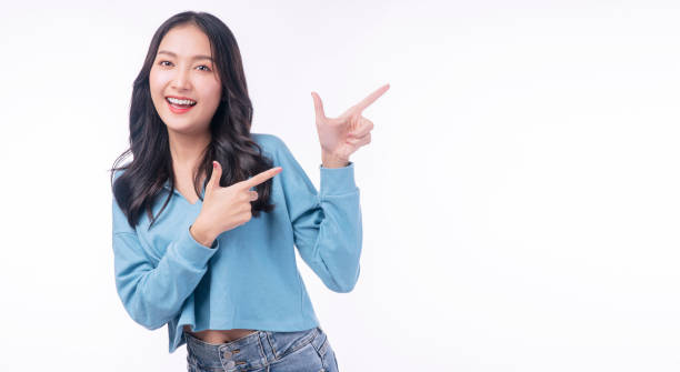 istock Cheerful excited asian woman use finger pointing to side with product or empty copy space standing over isolated white background. Model young girl laughing promotion. Advertisement presenting concept 1436664192