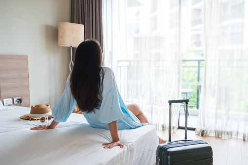 Carefree young Asian traveler woman relax on bed in hotel room. Travel alone, summer weekend, holiday concept. Copy space