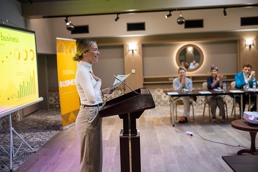 A young Caucasian woman speaking into a microphone at a business conference