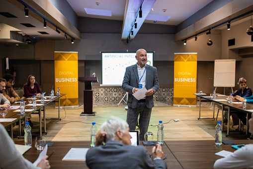 Speaker giving a talk in conference hall at business meeting event. Rear view of unrecognizable people in audience at the conference hall. Business and entrepreneurship concept.