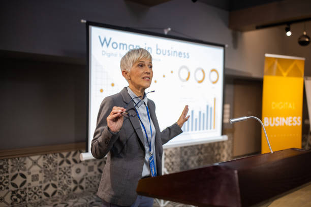 Businesswoman holding a speech for an audience in the conference room of a hotel A senior businesswoman holding a speech for an audience in the conference room of a hotel projector screen classroom stock pictures, royalty-free photos & images