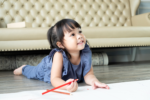 Beautiful Asian toddler girl 3 years old enjoy drawing and learning how to write in the living room at home. Preschool learning activity concept.