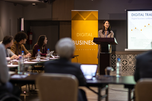 Low angle view of confident young woman in formalwear standing at the tribune and smiling while making a presentation with projection screen in the background