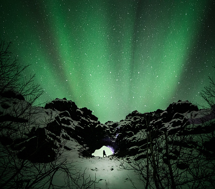 A silhouette of a girl watching the aurora borealis. Wonderful view of the green lights of the Aurora borealis over the snow- capped mountains.