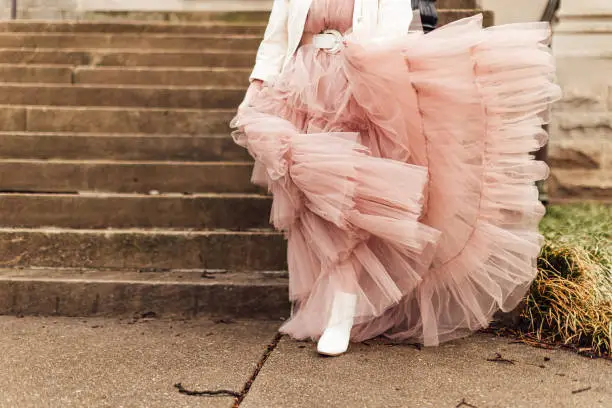 A closeup shot of an anonymous female wearing a pink tulle dress and leaning on the stairs