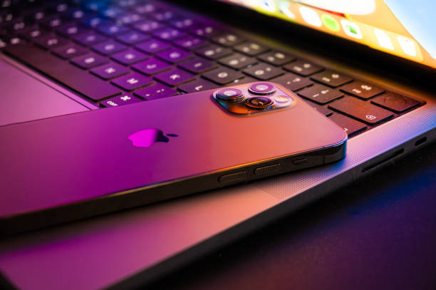 macbook pro 2021 w połowie otwarty z iphonem 13 podświetlanym przez wyświetlacz retina - macbook zdjęcia i obrazy z banku zdjęć