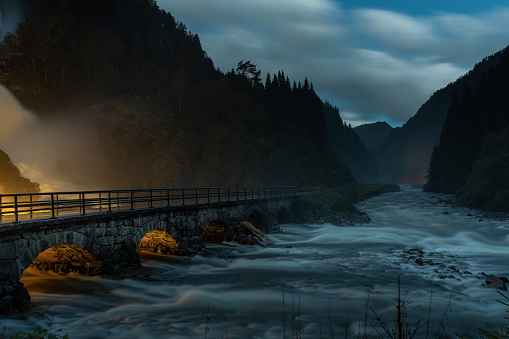 An eerie view of a bridge over the river in the evening at the bottom of hills