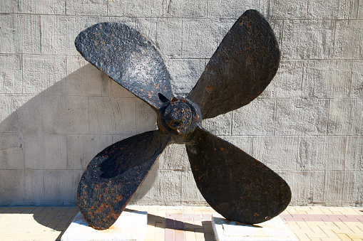 An old rusty four blade ship propeller leaning against a wall