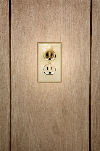 A vertical closeup shot of the broken electrical outlet on a wooden wall