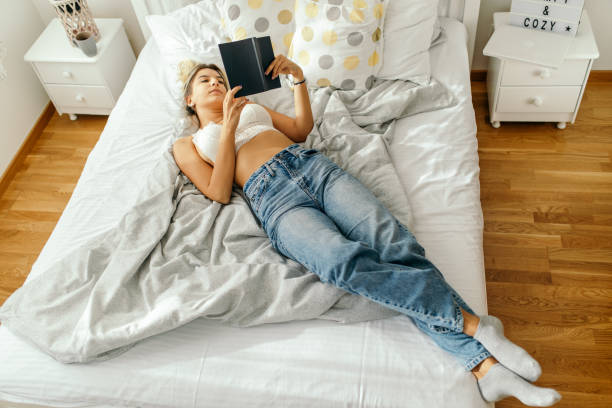istock Young woman reading book on bed at home 1436676859