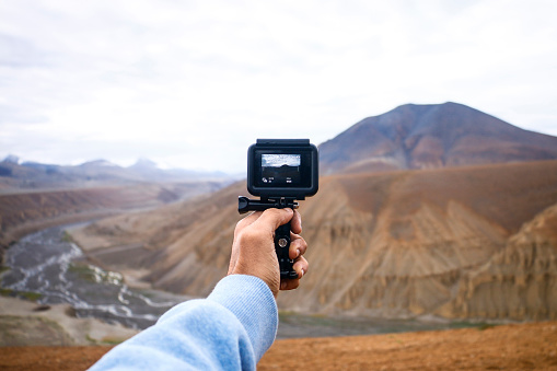 A person holding a camera in his hand taking a picture of the beautiful mountainous landscape