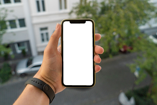 Man hand holding a smartphone similar to an iPhone X with a blank copy space outdoors