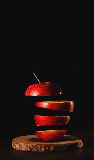 A vertical shot of red apple slices floating in the air isolated on a black background