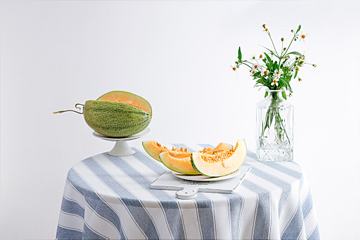 A still life photo of melon slices and flowers in a vase on a round table