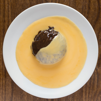 A top view of chocolate sponge pudding with custard on a wooden table surface