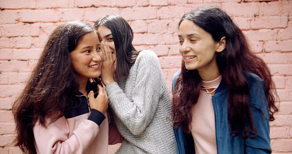 A portrait of three young pretty Indian girls gossiping and laughing against a brick wall background