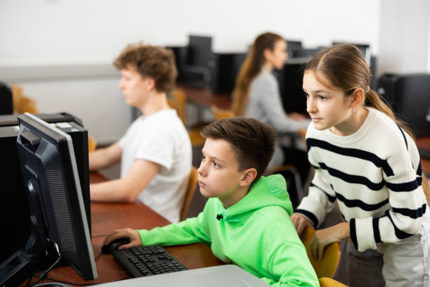 istock Teen schoolgirl helping focused classmate sitting at computer in class 1436684529