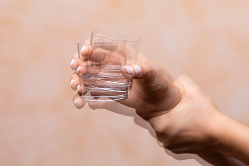 Closeup view on the shaking hand of a person holding drinking glass suffering from Parkinson's disease